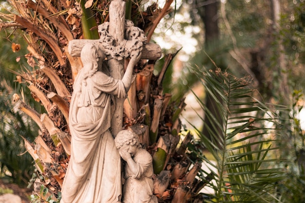 statua religiosa figura di un bambino e di sua madre accanto a una croce in un cimitero all'aperto