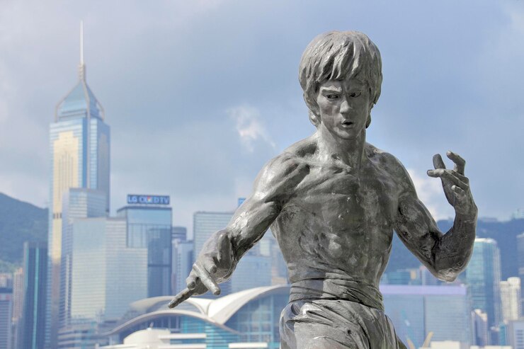 Photo statue of bruce lee on victoria harbor by modern buildings against sky