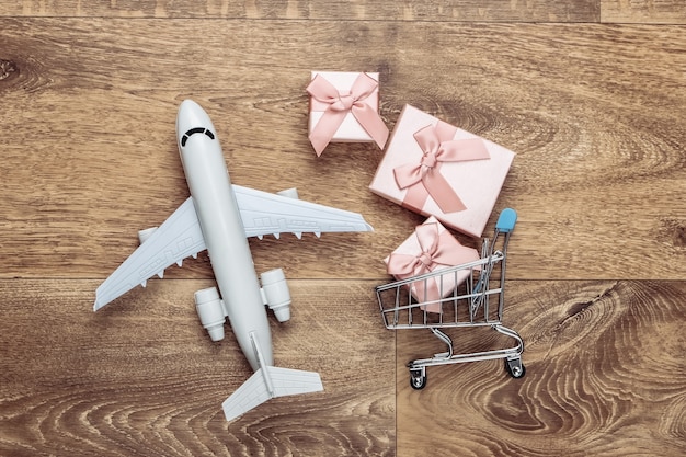 Statuetta di aereo, carrello della spesa e scatole regalo sul pavimento di legno. Lay piatto.