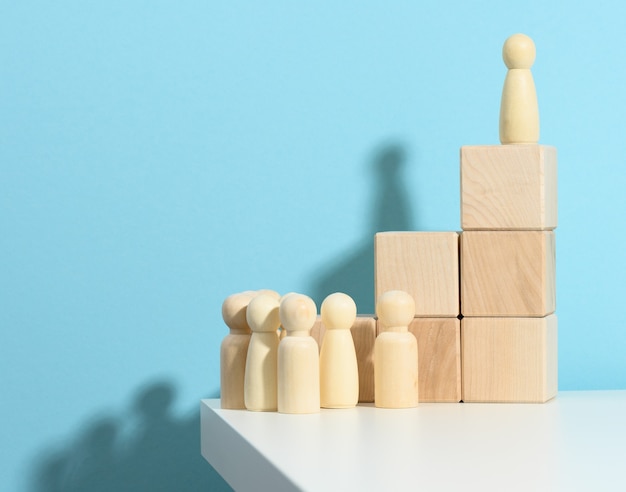 Statuetta di legno di un uomo si erge su un alto podio di cubi, sotto la folla. Ricerca di dipendenti di talento, raduno, manipolazione delle masse, selezione di dipendenti per la squadra