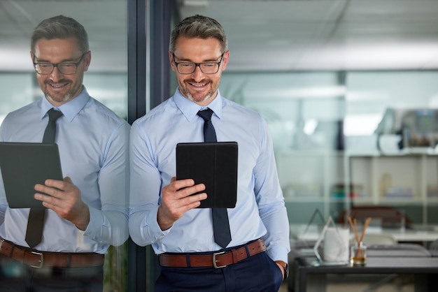 Stavamo andando verso le stelle Inquadratura di un uomo maturo che usa la sua tavoletta digitale mentre è appoggiato alla finestra dell'ufficio al lavoro