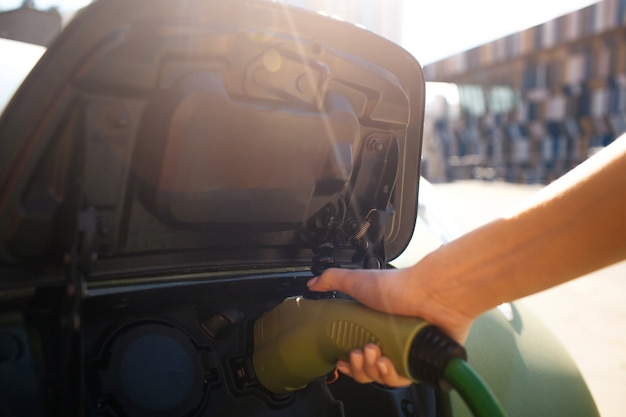 Stazione di ricarica per veicoli elettrici. Mano maschio che carica un'auto elettrica con il cavo di alimentazione collegato. Auto ecologica per un ambiente pulito