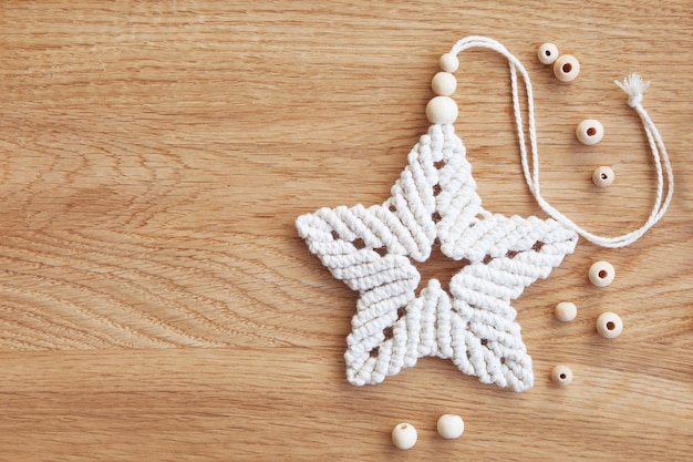 Stella di natale macramè in colore naturale e barbe di legno su un tavolo di legno. Macrame decorativo in corda di cotone. Passatempo donna. Concetto di Natale, inverno e capodanno