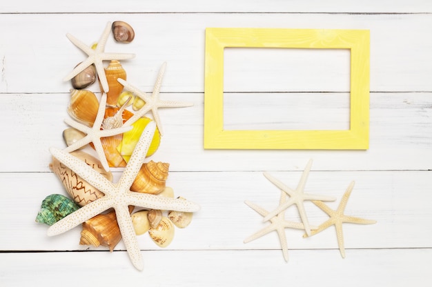 Stella di pesce, conchiglie e cornice in legno giallo su fondo di legno bianco.