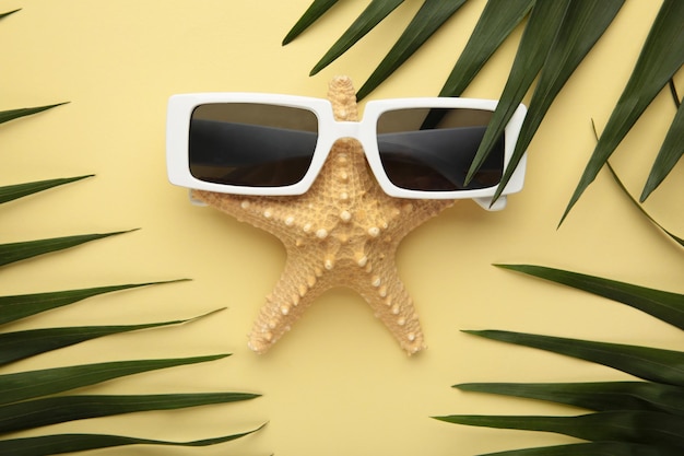Stelle marine in occhiali da sole con foglie di palma su sfondo beige Concetto di viaggio estivo