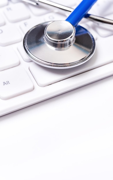 Stetoscopio blu sulla tastiera del computer su sfondo bianco del tavolo Concetto di tecnologia di trattamento delle informazioni mediche online primo piano spazio di copia macro