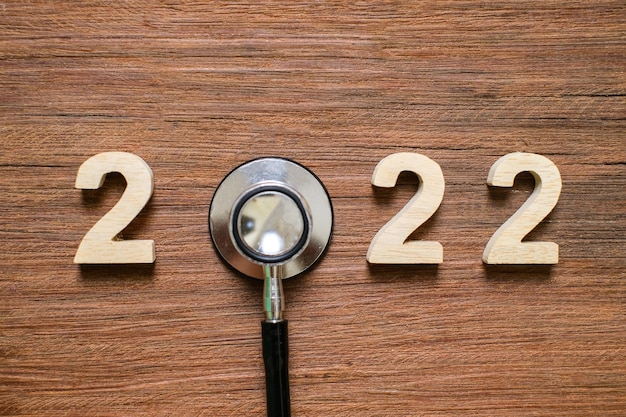 Stetoscopio della tenuta della mano con il numero 2022 su fondo blu. Felice anno nuovo per l'assistenza sanitaria, l'assicurazione, il benessere e il concetto medico