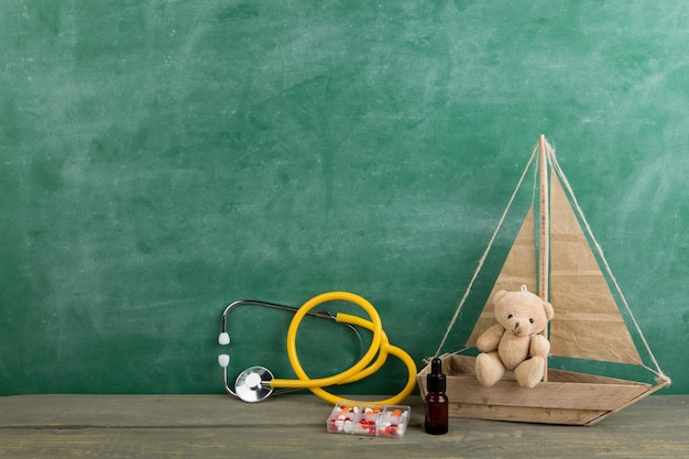Stetoscopio e farmaci dell'orso del giocattolo del posto di lavoro del podologo sul concetto di assistenza sanitaria dei bambini della scrivania di legno