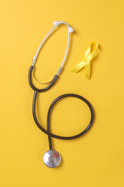 Stetoscopio e nastro in oro giallo. Consapevolezza del sarcoma, cancro alle ossa, consapevolezza del cancro infantile.