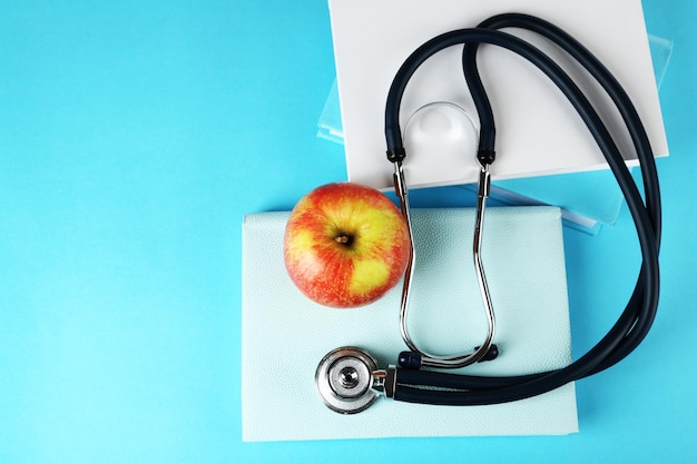 Stetoscopio medico con mela e libri su sfondo blu