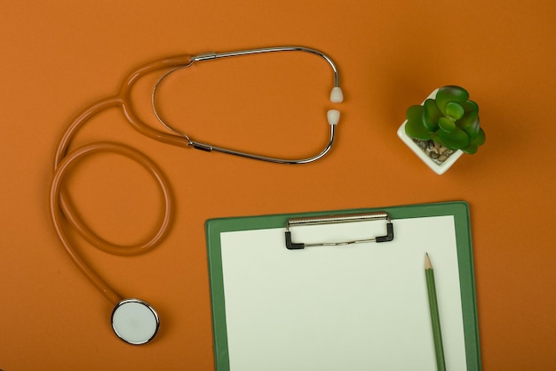 Stetoscopio medico sul posto di lavoro arancione e appunti vuoti su sfondo di carta arancione