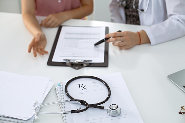 Stetoscopio, modulo di prescrizione medica giacciono sullo sfondo di un medico e un paziente che discutono dei risultati dell'esame sanitario.