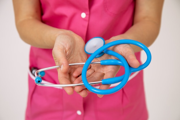 Stetoscopio nelle mani della dottoressa in uniforme medica rosa. Assicurazione sulla vita e sulla salute. Esami professionali. Medicina e salute. Uno stile di vita sano. Medicina moderna. Cure mediche.