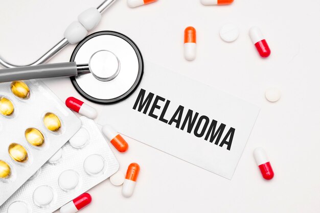 Stetoscopio, pillole e taccuino con la parola melanoma sulla scrivania medica.