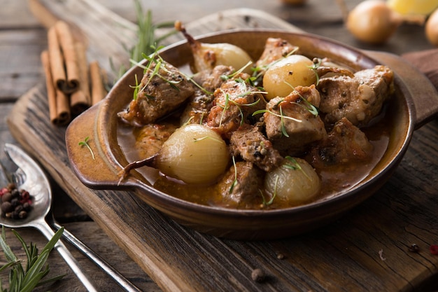 Stifado - delizioso stufato di manzo mediterraneo con bulbi di cipolla, cannella e spezie in una casseruola, su un tavolo di legno nero, vista dall'alto, primo piano