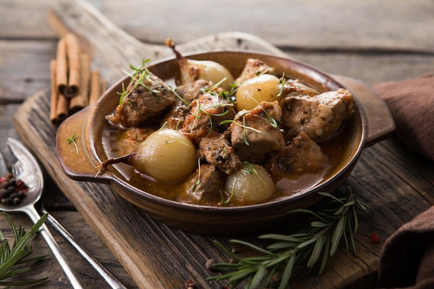 Stifado - delizioso stufato di manzo mediterraneo con bulbi di cipolla, cannella e spezie in una casseruola, su un tavolo di legno nero, vista dall'alto, primo piano