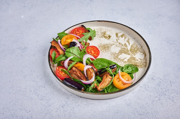 Stile casalingo insalata con melanzane fritte, pomodori, rucola, spinaci, lattuga e salsa su un piatto di ceramica