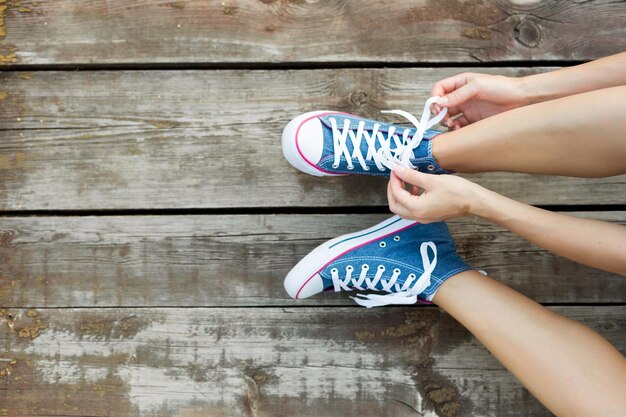 Stile di vita all'aperto primo piano delle gambe della bella ragazza giovane Donna giovane donna che lega i lacci delle sue scarpe da ginnastica di jeans seduta sul pavimento di legno