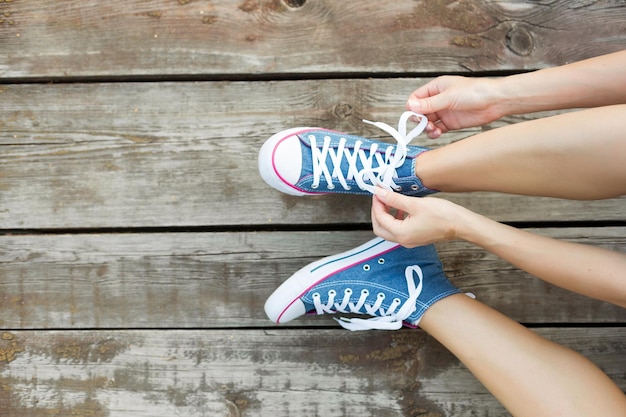 Stile di vita all'aperto primo piano delle gambe della bella ragazza giovane Donna giovane donna che lega i lacci delle sue scarpe da ginnastica di jeans seduta sul pavimento di legno