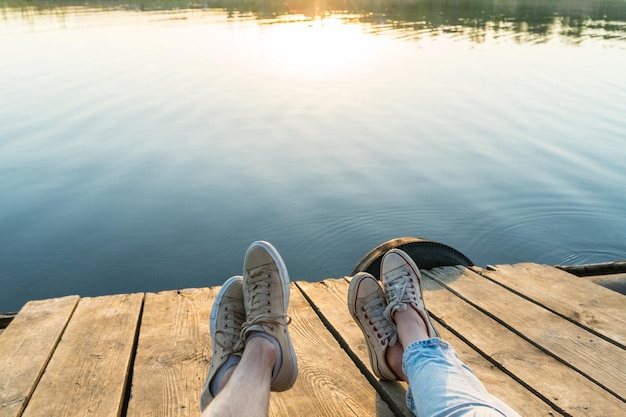 Stile di vita all'aperto vista di una coppia che indossa scarpe da ginnastica seduta su un molo di legno all'acqua su un tramonto