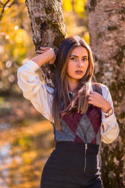 Stile di vita autunnale, una giovane bruna caucasica, studentessa universitaria in un parco vicino a un albero con uno sguardo dolce