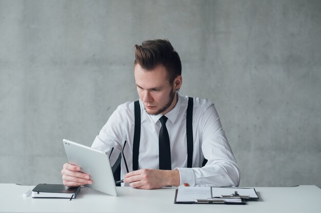 Stile di vita aziendale. Ritratto di giovane responsabile dell'ufficio seduto alla scrivania, utilizzando tablet. Espressione facciale seria. Copia spazio.