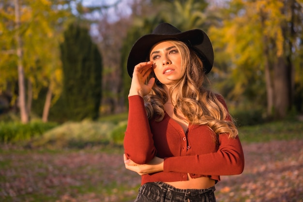 Stile di vita bionda ragazza caucasica in un maglione rosso e un cappello nero godersi la natura in un parco con alberi in un bellissimo ritratto di autunno del giovane modello sorridente