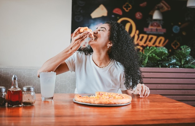 Stile di vita di una donna dai capelli afro che gusta una pizza in un ristorante Donna felice con i capelli afro che mangia pizza in un ristorante