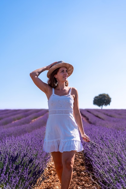 Stile di vita di una donna sorridente in un campo estivo di lavanda che indossa un abito bianco con un cappello