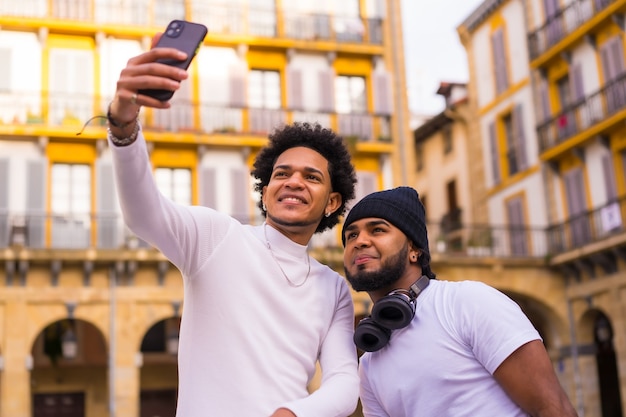 Stile di vita, due amici neri latini che si fanno un bel selfie per strada. Ragazzo con capelli afro e ragazzo con cappello e auricolari