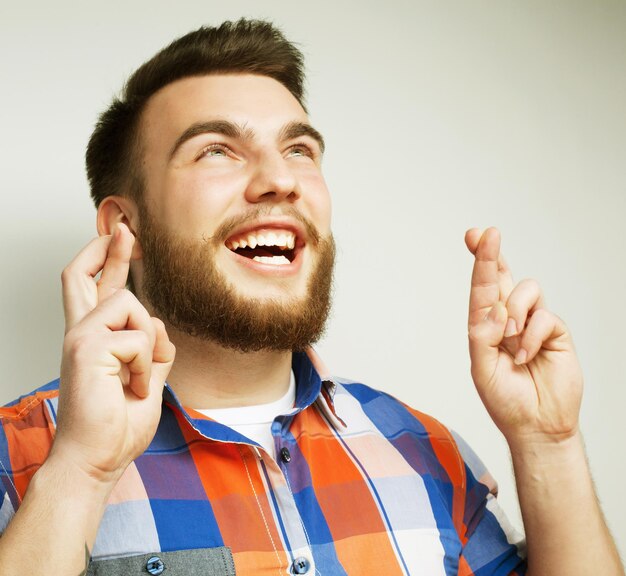 stile di vita e concetto di persone Aspettando un momento speciale Ritratto di un giovane uomo barbuto in camicia che tiene le dita mentre si trova su uno sfondo bianco stile hipster ed emozioni positive