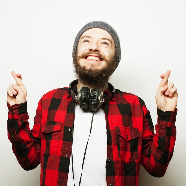 Stile di vita e concetto di persone: in attesa di un momento speciale. Ritratto di giovane uomo barbuto in camicia che tiene le dita in piedi su sfondo bianco. Stile hipster ed emozioni positive.