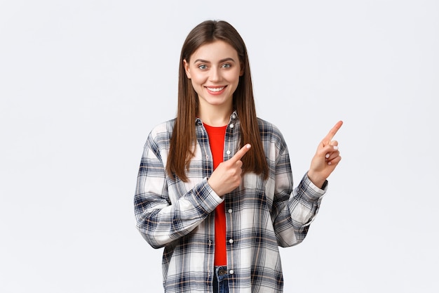 Stile di vita, emozioni diverse, concetto di attività per il tempo libero. Una ragazza caucasica attraente dall'aspetto amichevole con una camicia a quadri informa sulle nuove promozioni, puntando il dito a destra e sorridendo alla telecamera.