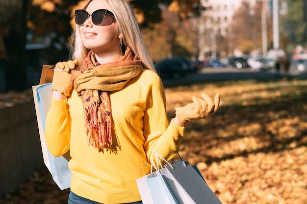 Stile di vita fashionista. Signora felice che cammina con le borse della spesa, godendo la giornata di sole autunnale.