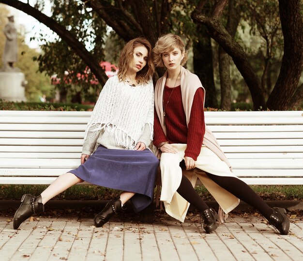 Stile di vita, felicità, emozioni e concetto di persone: belle giovani donne sedute su una panchina nel parco autunnale