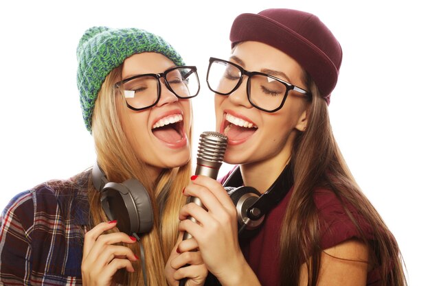 Stile di vita, felicità, emozioni e concetto di persone: due ragazze hipster di bellezza con un microfono che cantano e si divertono