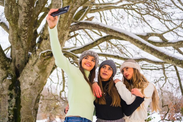 Stile di vita invernale, tre bellissimi amici caucasici che prendono un selfie con il telefono nella neve sotto un albero, vacanze nella natura