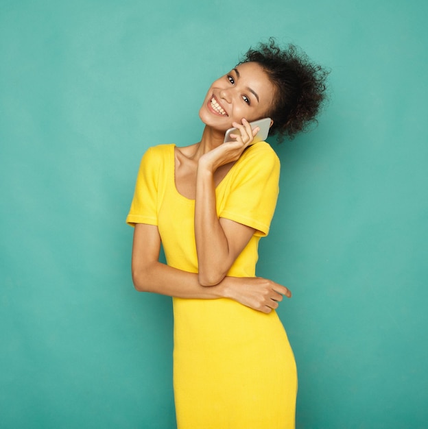 Stile di vita moderno e comunicazione. Sorridente bella donna afro-americana che parla al telefono, sfondo blu studio