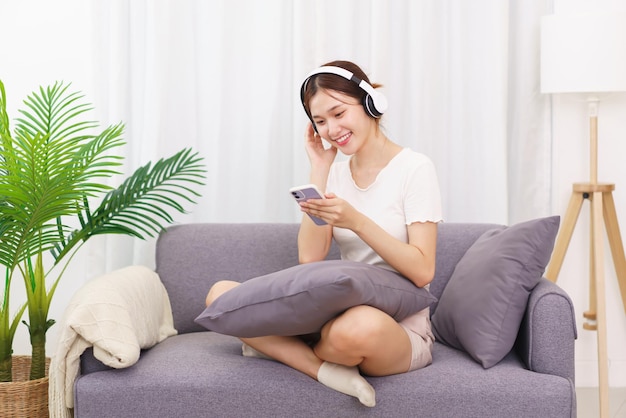 Stile di vita nel concetto di soggiorno Giovane donna asiatica in cuffia per ascoltare musica sullo smartphone