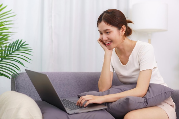 Stile di vita nel concetto di soggiorno Giovane donna asiatica seduta con la mano sul mento e utilizzando il laptop