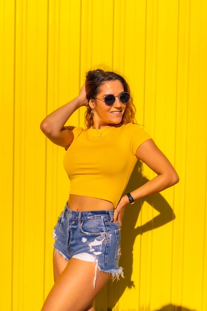 Stile di vita, ragazza bionda caucasica in magliette gialle e jeans corti su una parete gialla. Posa alla moda con un sorriso