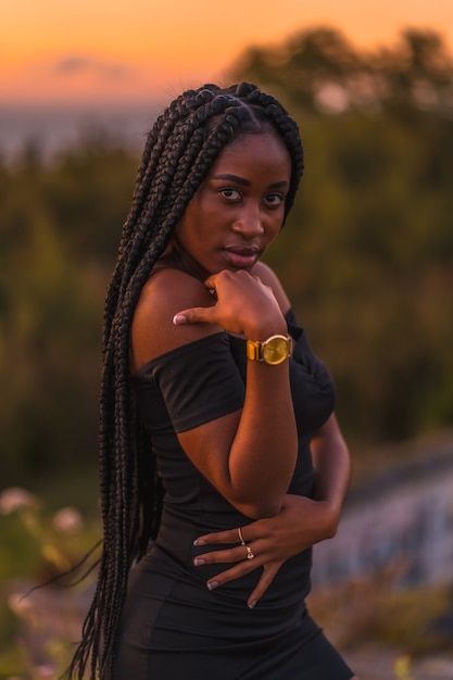 Stile di vita ragazza latina con la pelle nera con belle trecce lunghe tra i capelli che indossa un abito corto nero stretto