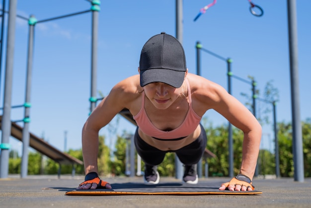 Stile di vita sano e attivo. Sport e fitness. Donna felice in abiti sportivi che si allena nel campo sportivo in una soleggiata giornata estiva, facendo flessioni