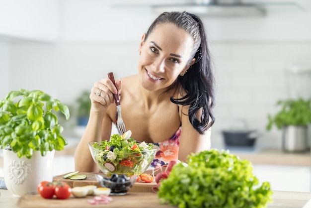 Stile di vita sano giovane donna che mangia insalata di lattuga Giovane bruna mangiare cibo sano nella sua cucina