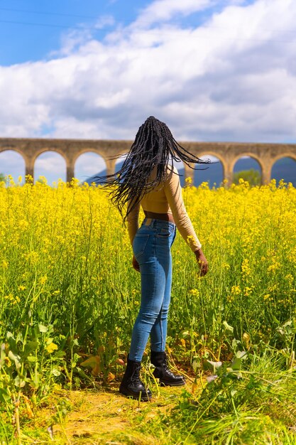 Stile di vita sorridente in natura una ragazza di etnia nera con trecce un viaggiatore in un campo di fiori gialli