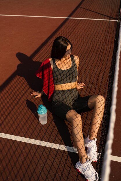 Stile di vita sportivo Ragazza sportiva con bottiglia d'acqua e asciugamano Modello asiatico seduto sul campo da tennis