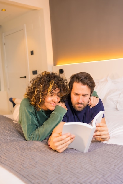 Stile di vita, una giovane coppia caucasica, in pigiama a letto a leggere un bel libro abbracciato