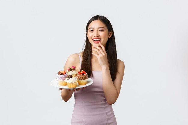 Stile di vita, vacanze, celebrazione e concetto di cibo. Bella giovane donna asiatica ospite della festa in abito da sera, trattando gli ospiti con deliziosi dessert