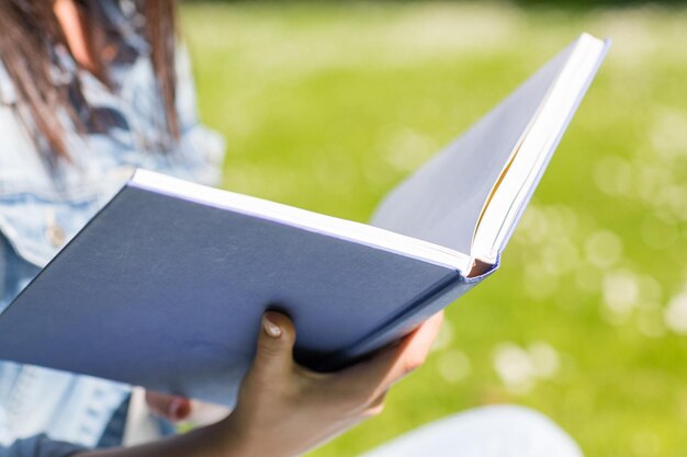 stile di vita, vacanze estive, istruzione, letteratura e concetto di persone - primo piano del libro di lettura della ragazza e seduto sull'erba nel parco