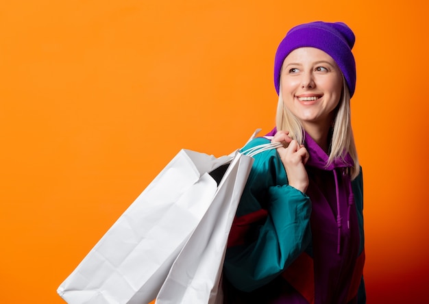 Stile donna in tuta anni '90 con borse della spesa su arancione